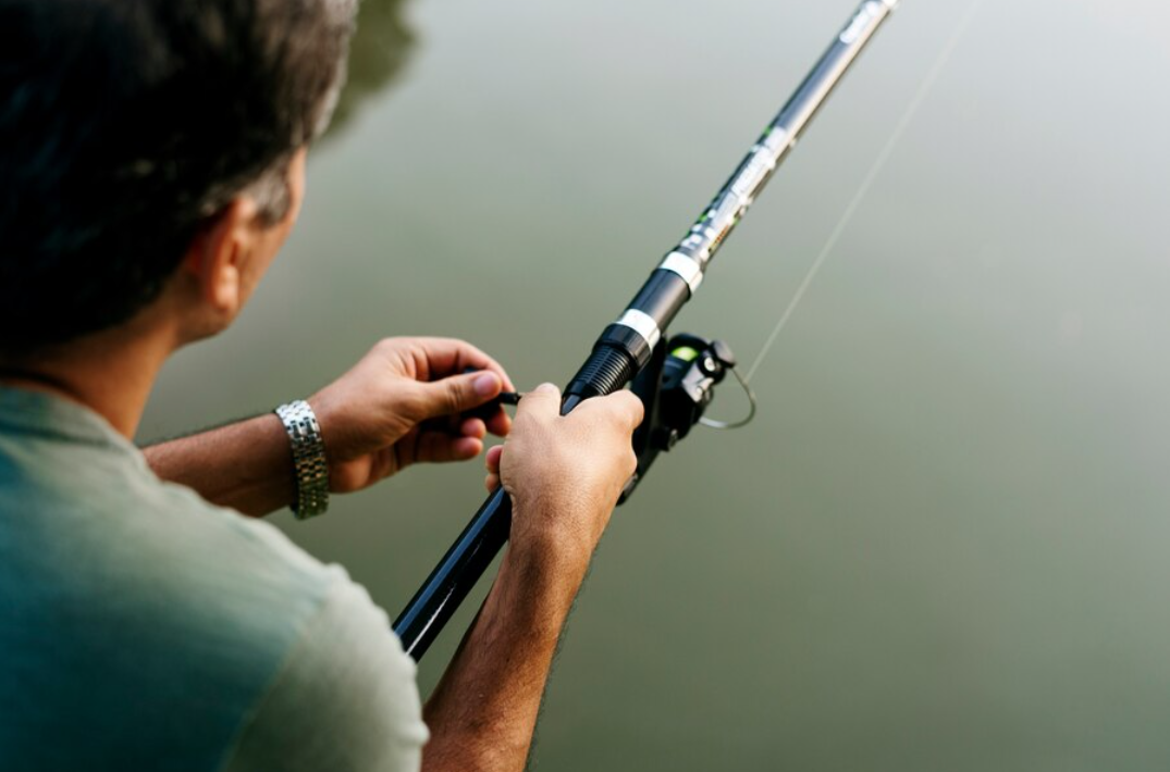 A person holding a fishing rod over calm water, preparing to fish.