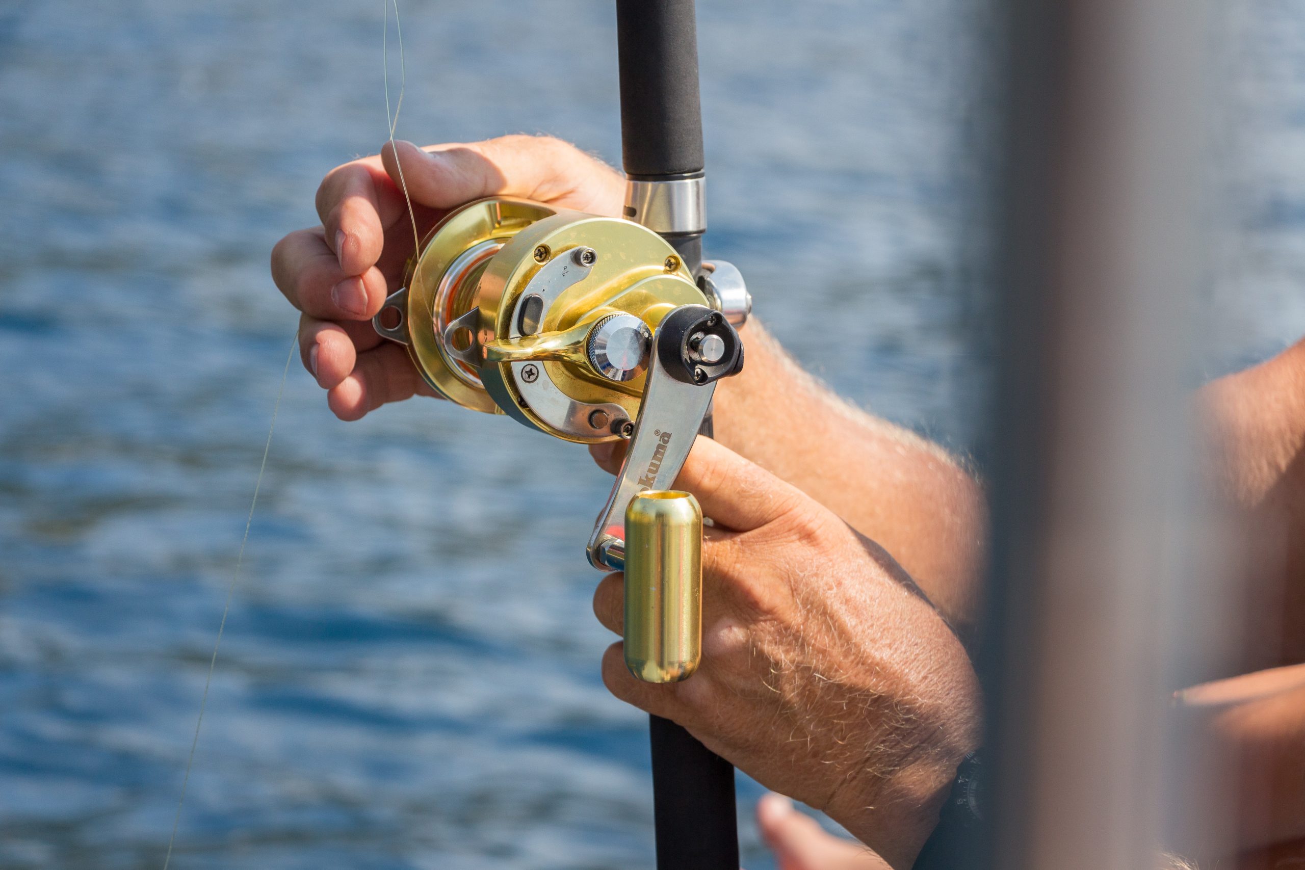 Sportfishing trip Close-up of hands holding a fishing rod and reel over water.