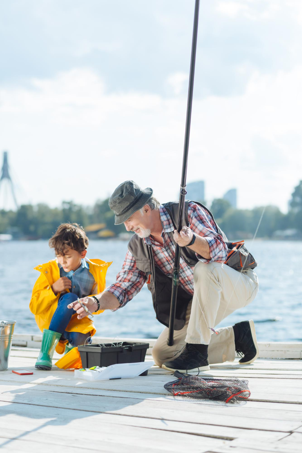 Older man and young boy fishing on a dock by the water, preparing gear on a sunny day.