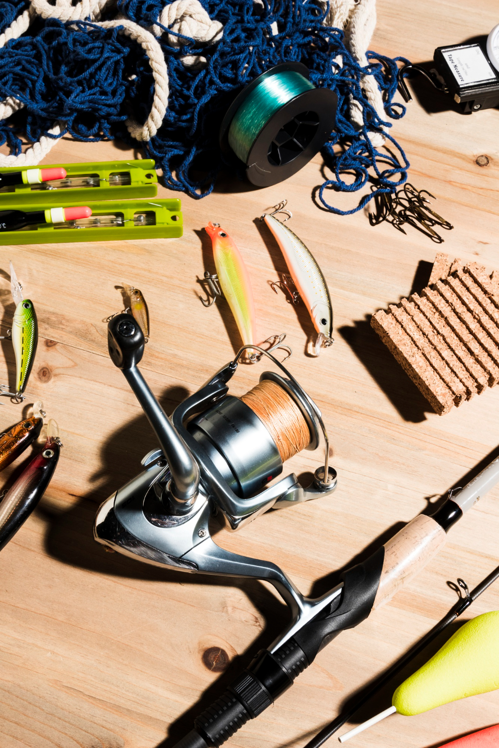 2148189313 Fishing gear, lures, a reel, hooks, and rope arranged on a wooden table in bright sunlight.