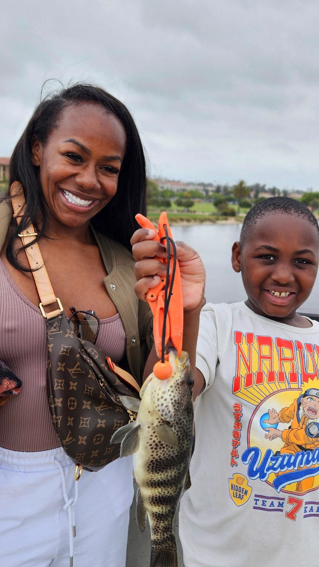Mother and Son Pier Fishing Smiling woman and boy proudly holding a freshly caught fish by the water on a cloudy day.