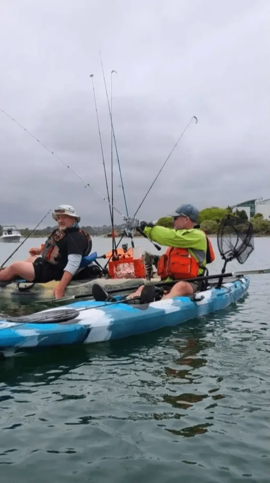 Two people in kayaks fishing on a calm lake with cloudy skies.