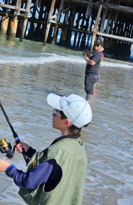 shoreline-fishing-3 Two people fishing in shallow water by a pier, both wearing hats and sunglasses.