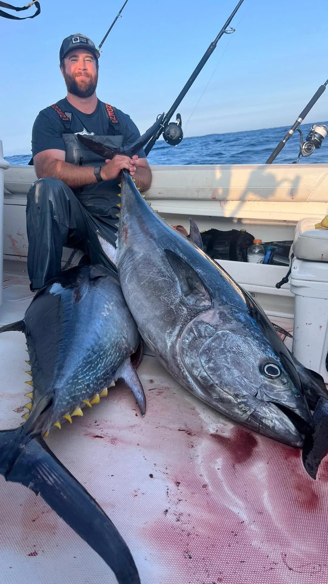 sports-fishing-4 A man on a boat holds a fishing rod, posing with two large tunas on the bloodstained deck.