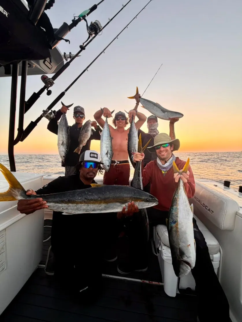tcs-landing-2 Five people on a boat holding large fish at sunset, smiling and posing for a photo after fishing.